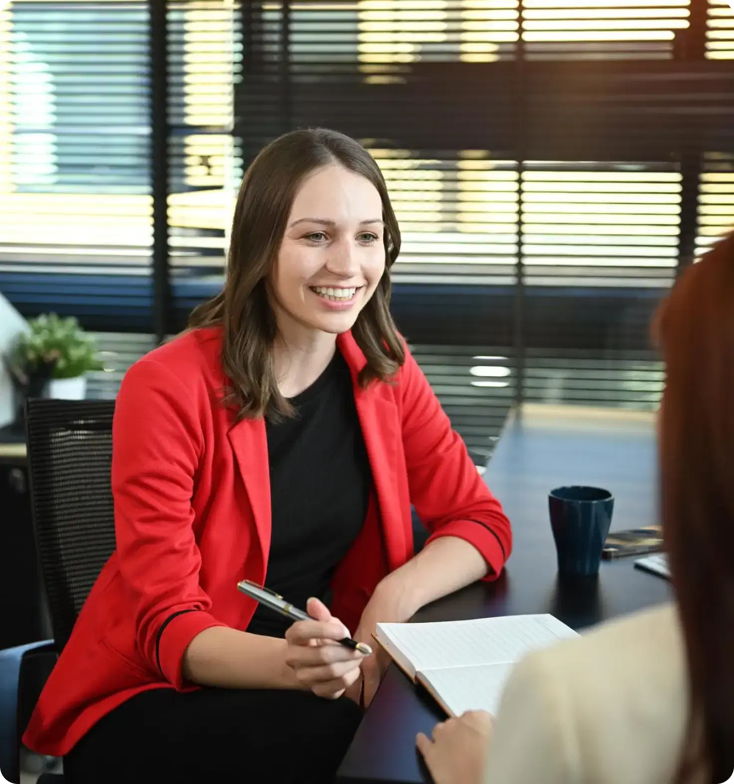 Two people talking across a desk in a sunlit meeting room