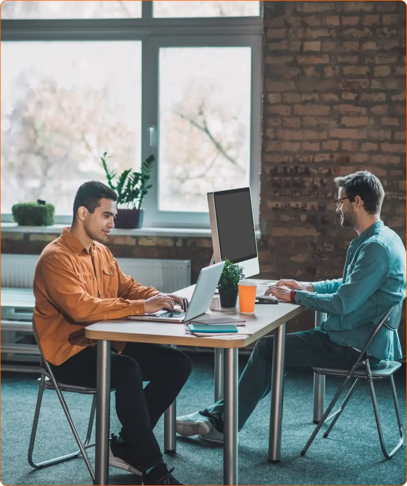 Two people working across a shared desk, one at a laptop